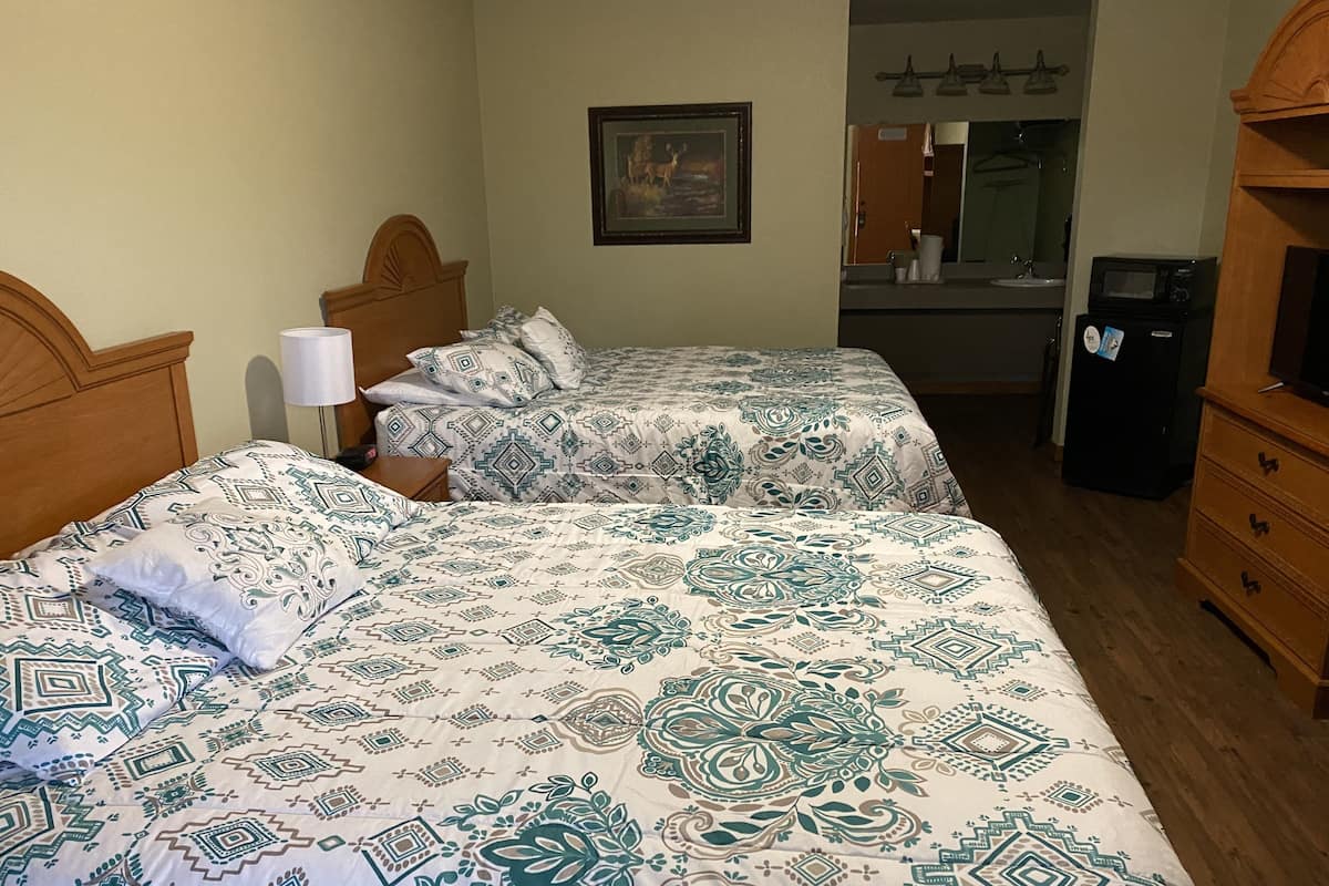 A hotel room with two beds, a nightstand, a lamp, a dresser, a microwave, and a framed picture on the wall.