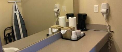 A hotel bathroom with a sink, mirror, towel rack, hairdryer, and toilet paper dispenser.