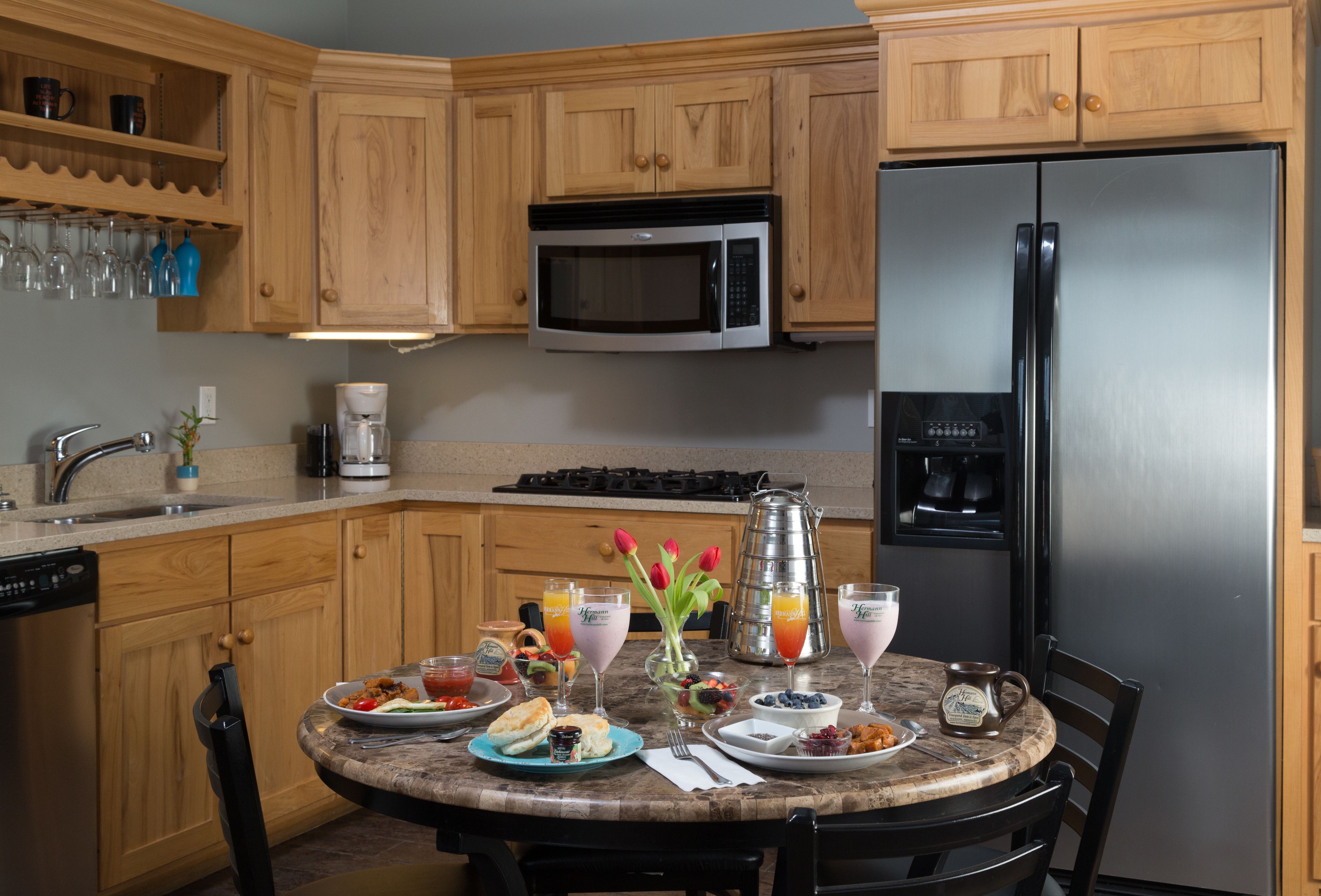 A kitchen with wooden cabinets, a stainless steel refrigerator, a microwave, and a dining table set with breakfast items.