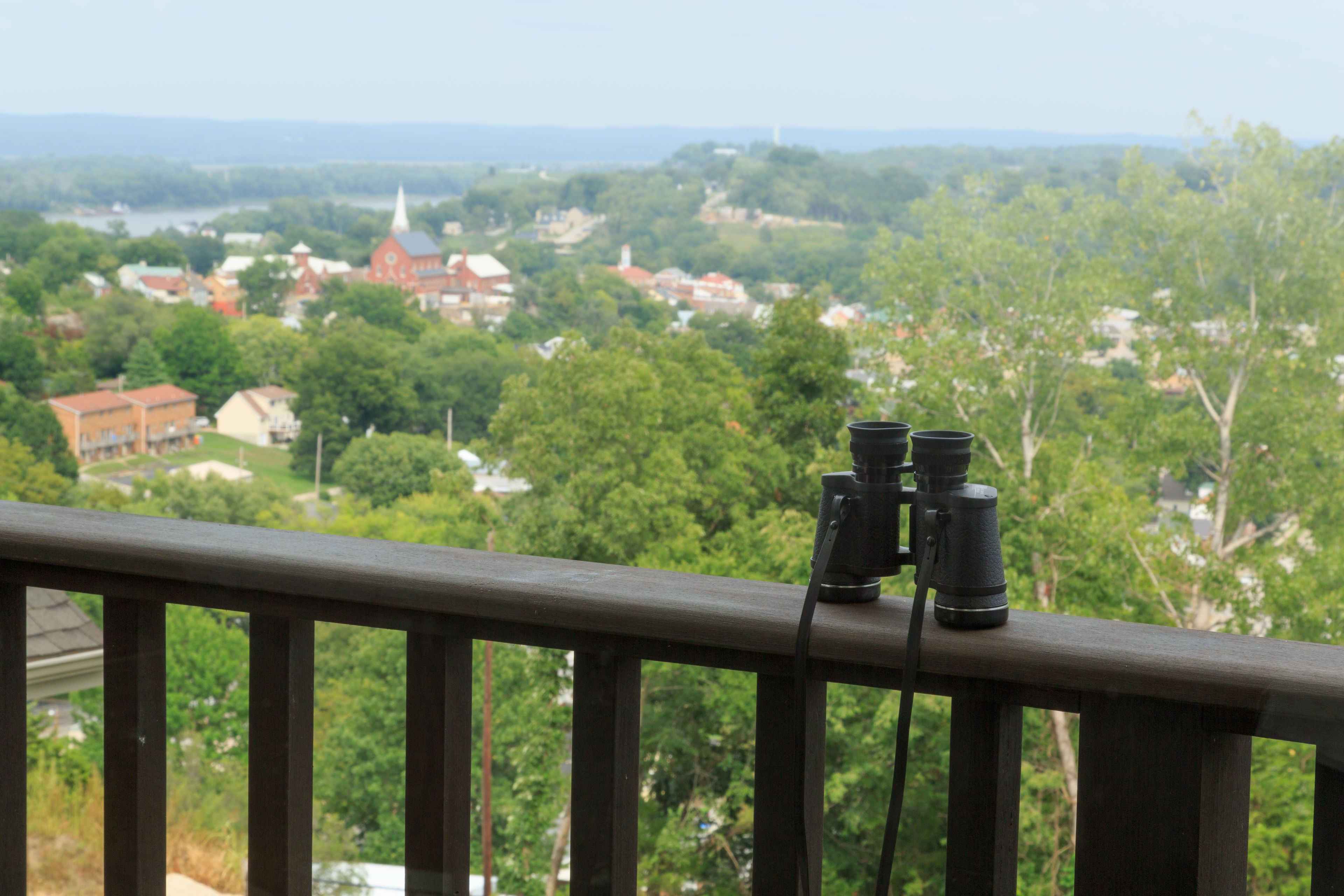 A balcony with binoculars overlooking a town with buildings and trees.