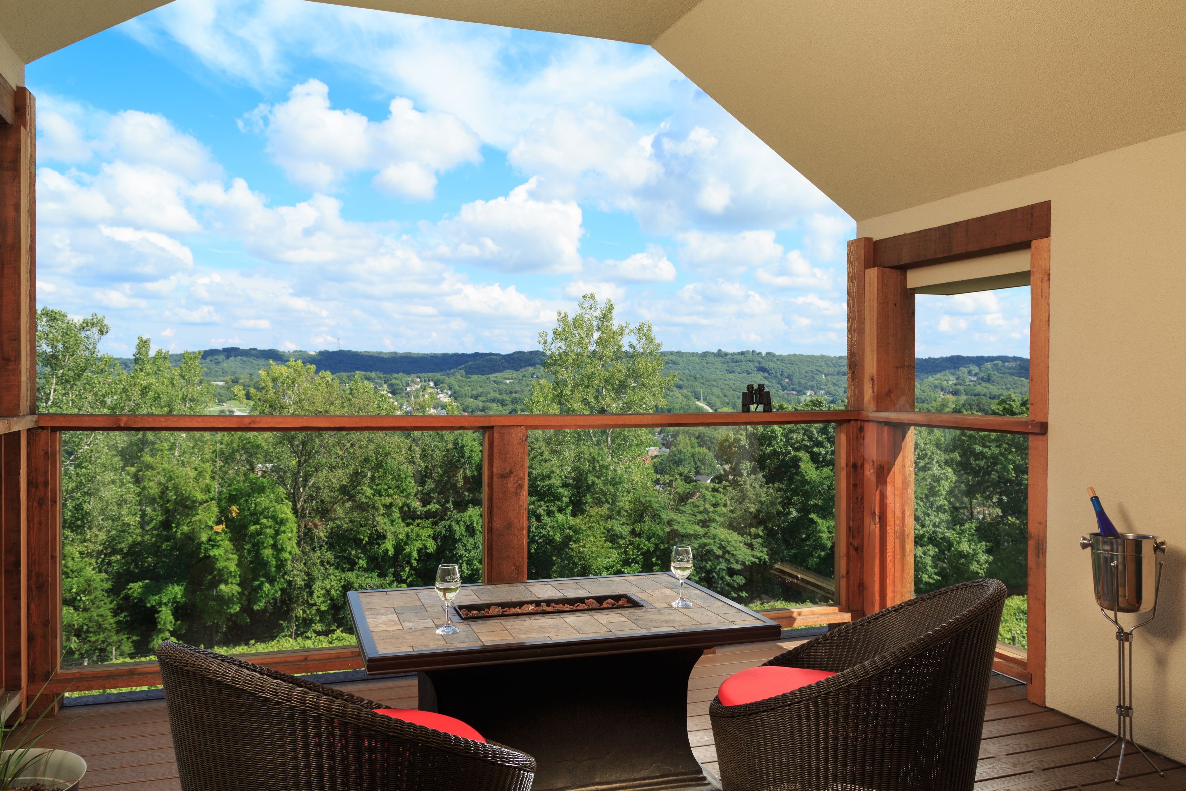 Un balcon agrémenté de meubles en osier, une table avec des verres et une vue sur un paysage boisé.