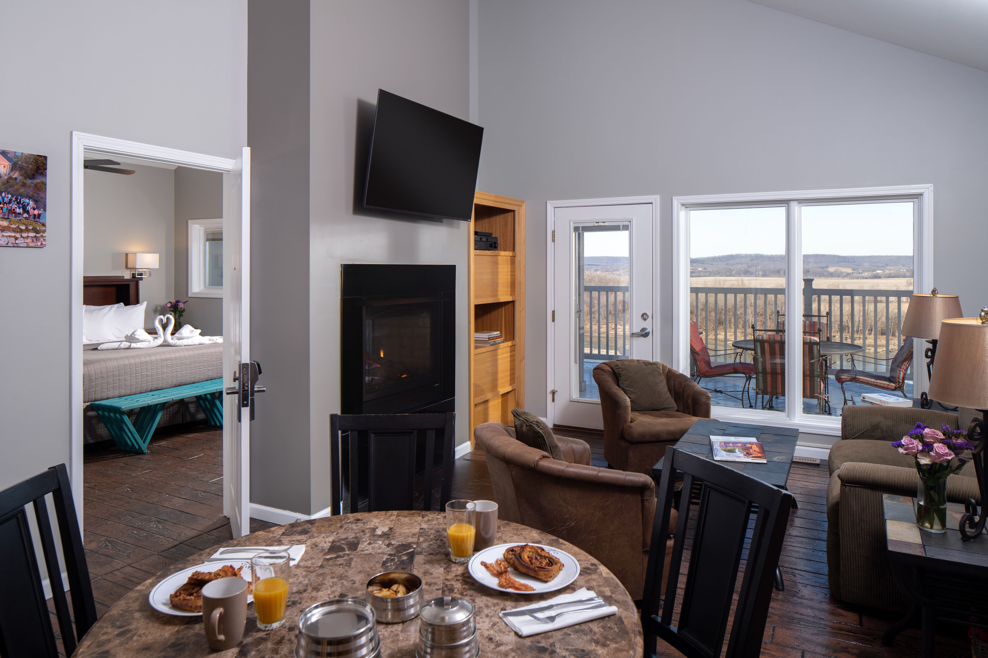 A spacious living area with a fireplace, a dining table set with breakfast, and a balcony with a view.