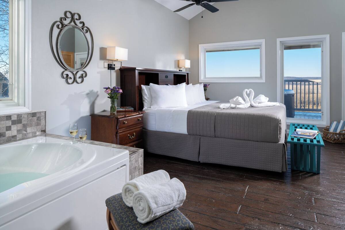 Habitación de hotel con una cama grande, un área de descanso con vistas, un baño con bañera y un ventilador de techo.