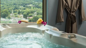 Un jacuzzi con vistas a un bosque, una escobilla para la ducha y una bata colgada en la pared.