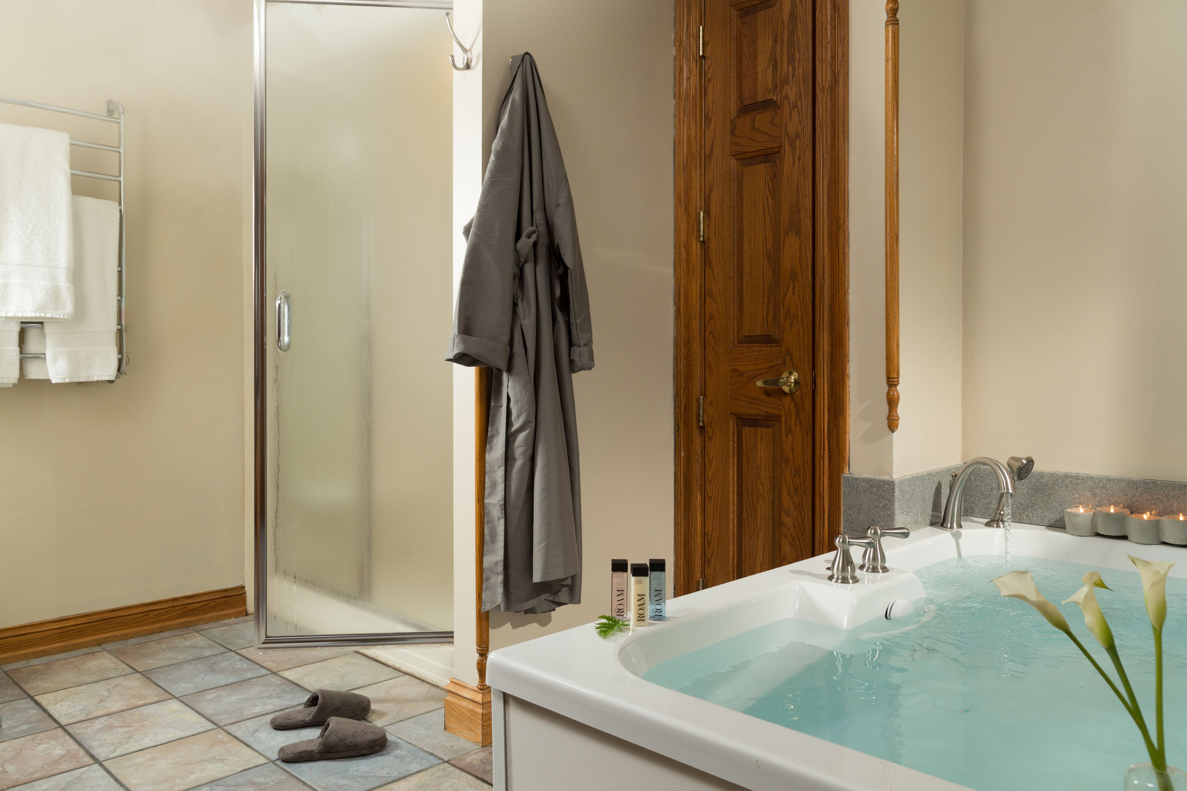 A bathroom with a bathtub, a glass shower door, towels, and toiletries.
