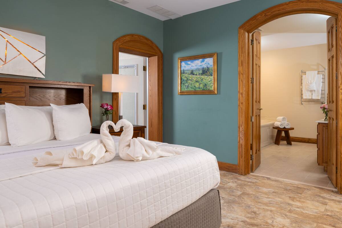Una habitación de hotel con cama, un cuadro y un baño visible a través de una puerta abierta.
