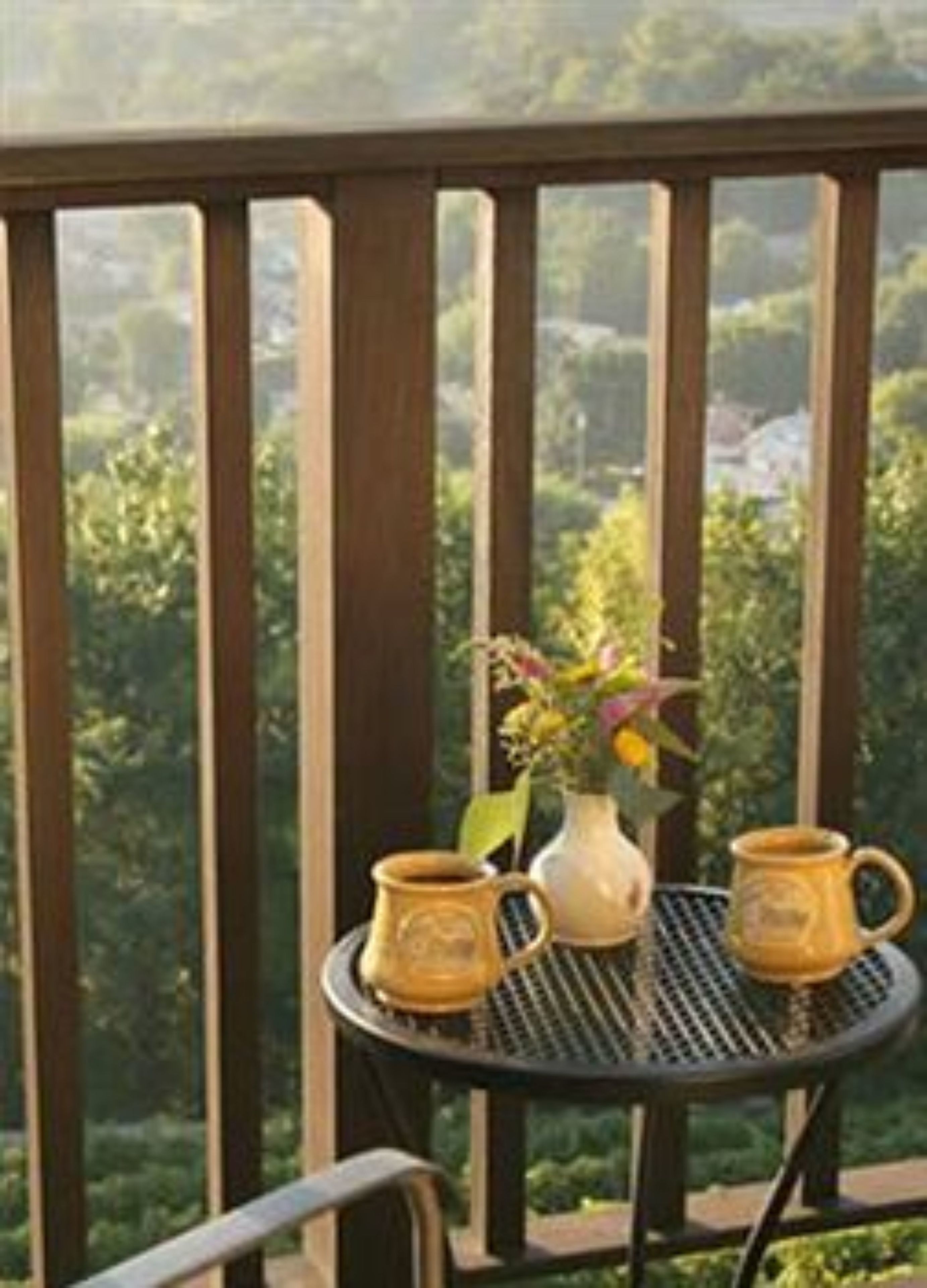 A balcony with a table, two mugs, and a vase with flowers.