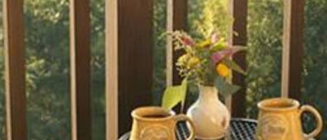 A balcony with a table, two mugs, and a vase with flowers.