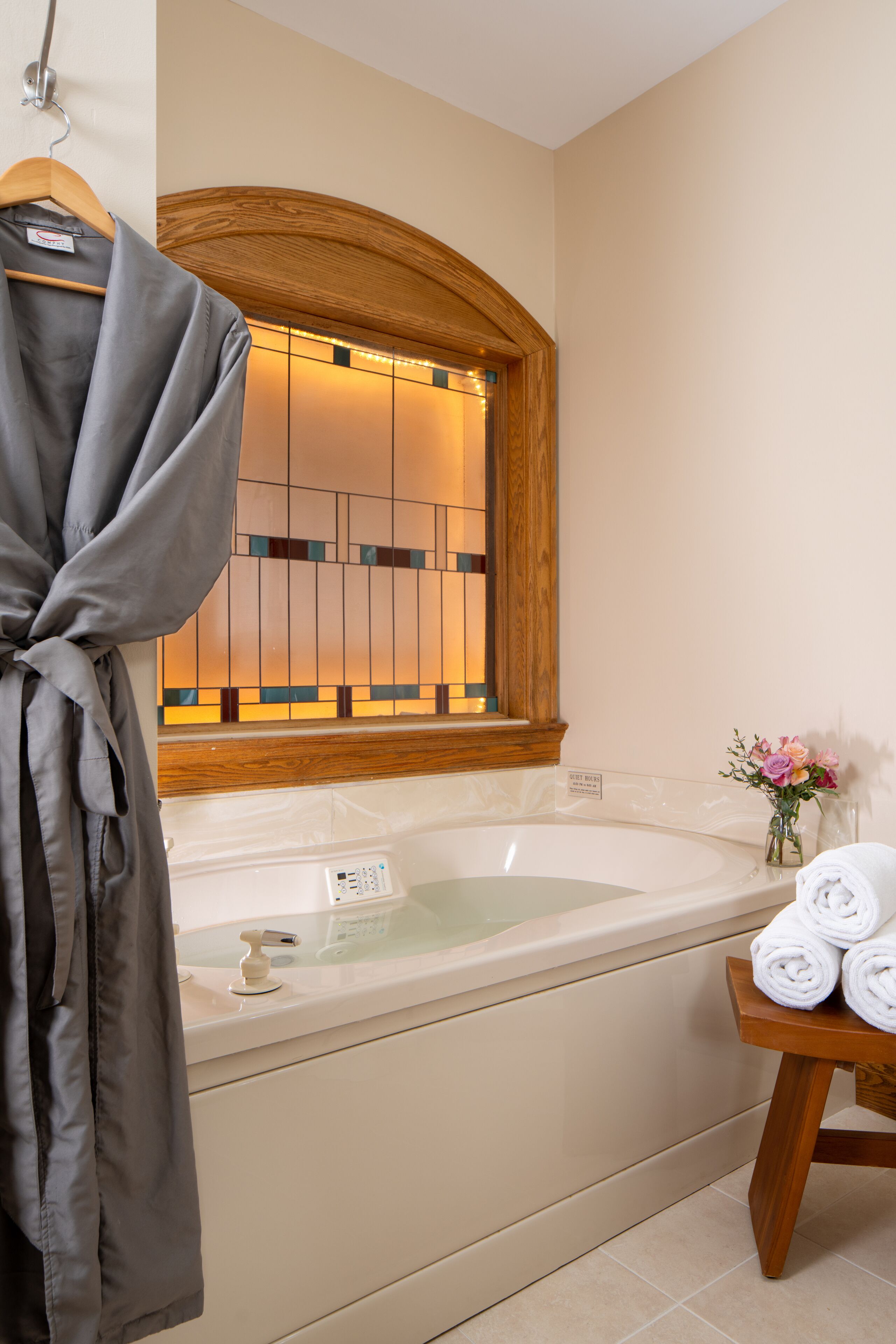 A bathroom with a bathtub, a wooden vanity, a robe hanging on a rack, and a vase with flowers.