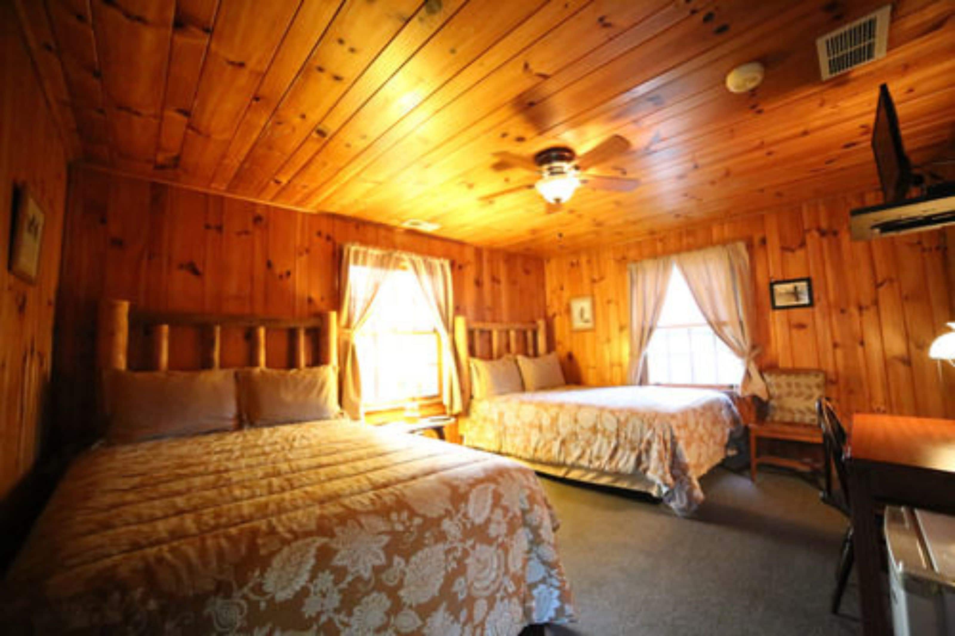 A wooden cabin room with two beds, a ceiling fan, and a small table.
