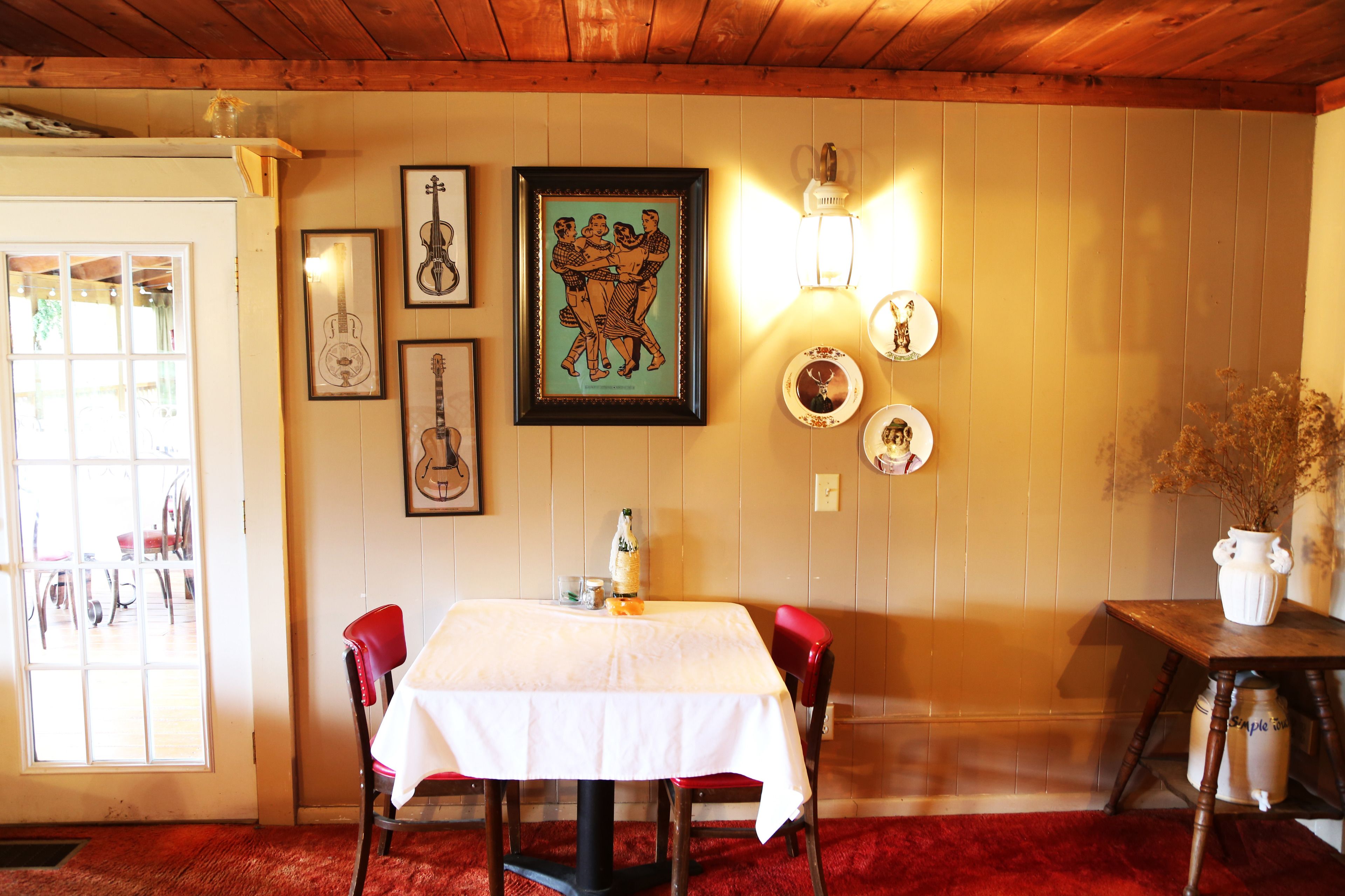 A dining area with a table set for two, framed artwork on the wall, and a wooden ceiling.