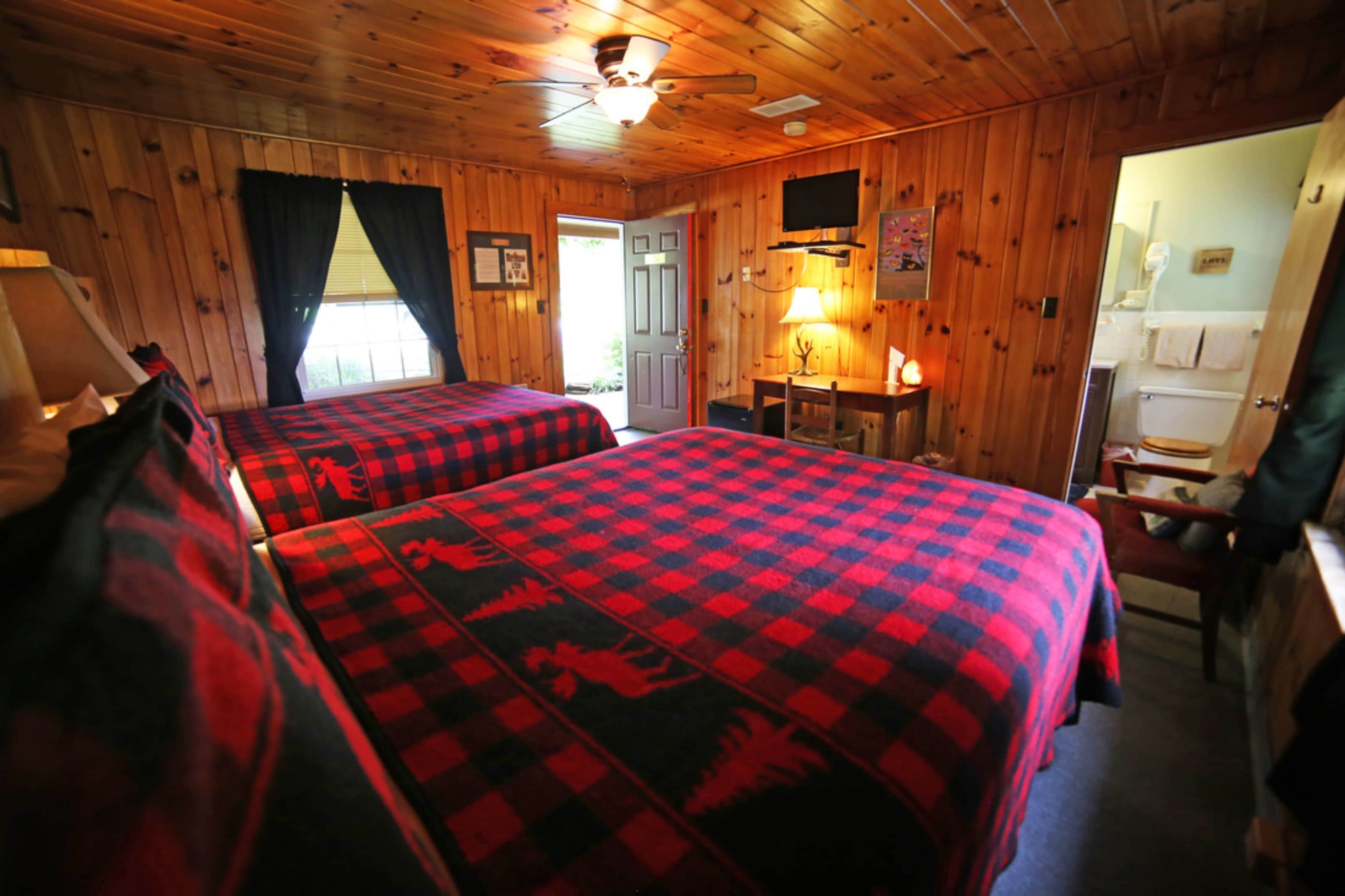 A room with two beds, a desk, a chair, a television, and a bathroom visible through an open door.