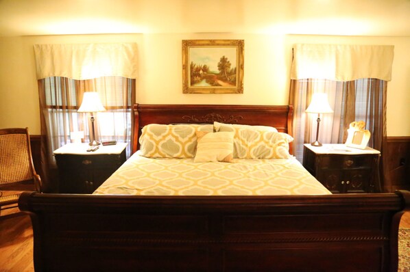 Una habitación de hotel con una cama grande, dos mesitas de noche, una lámpara sobre cada una, un cuadro en la pared y cortinas en las ventanas.