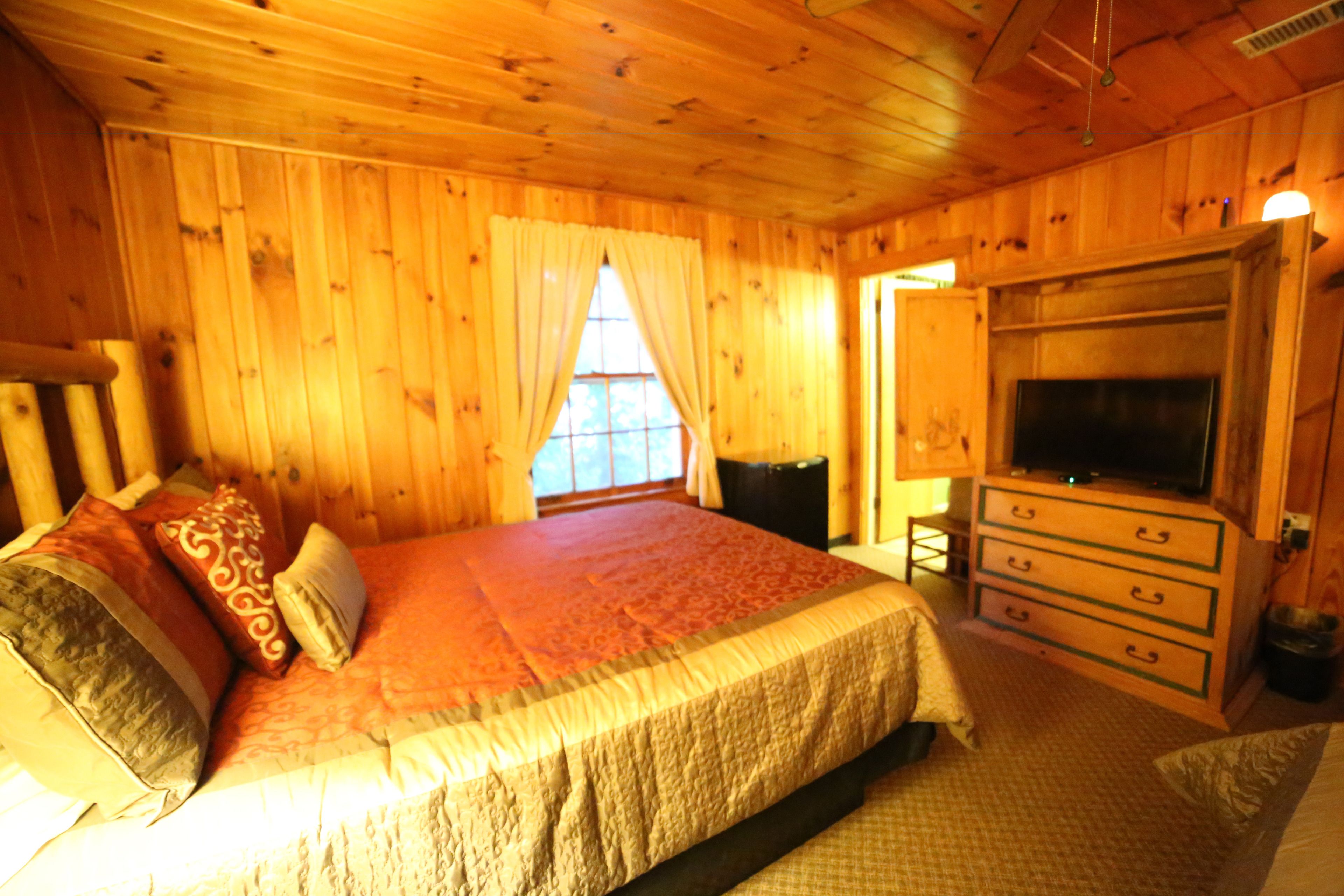 A wooden cabin bedroom with a bed, a dresser, and a television.
