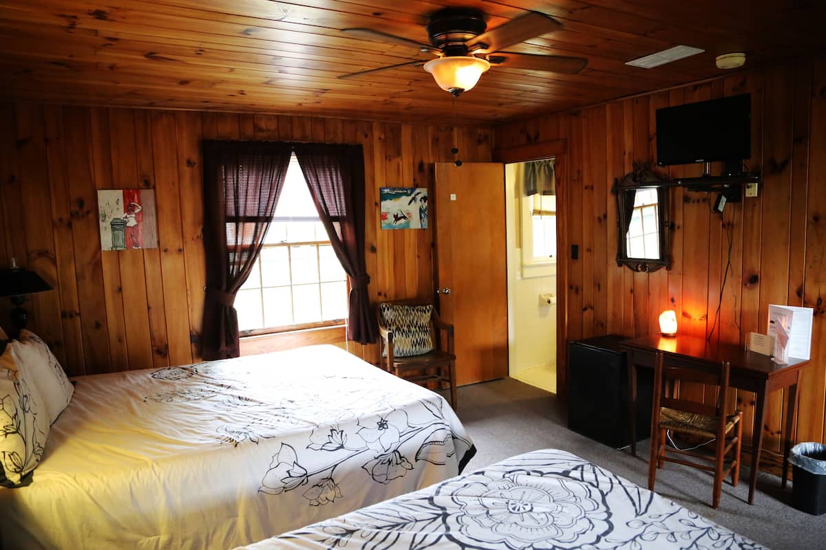 A wooden room with two beds, a desk, a chair, a television, and a ceiling fan.