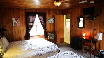 A wooden room with two beds, a desk, a chair, a television, and a ceiling fan.