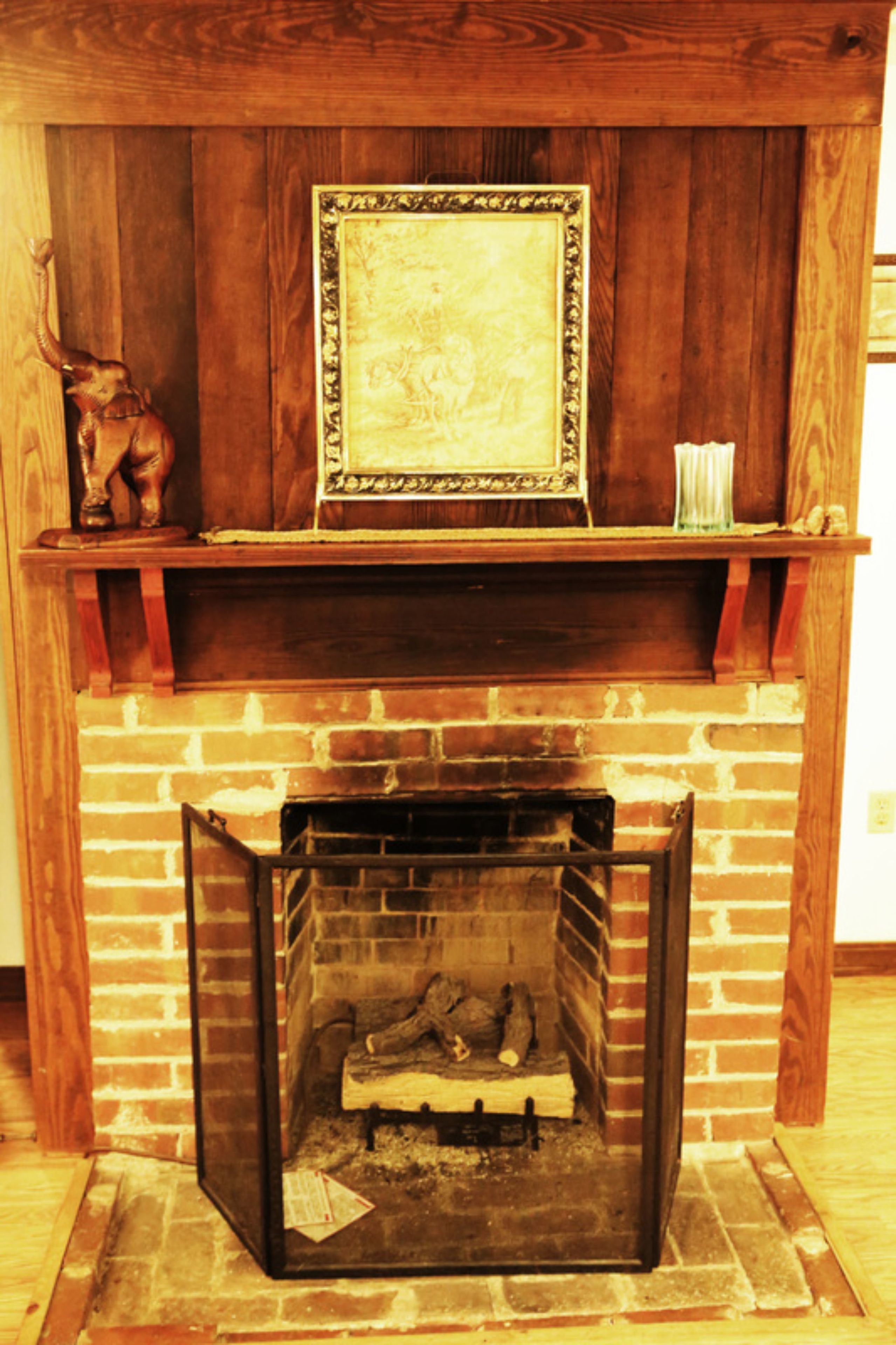 A fireplace with a framed picture above it, a shelf with decorative items, and a brick wall.