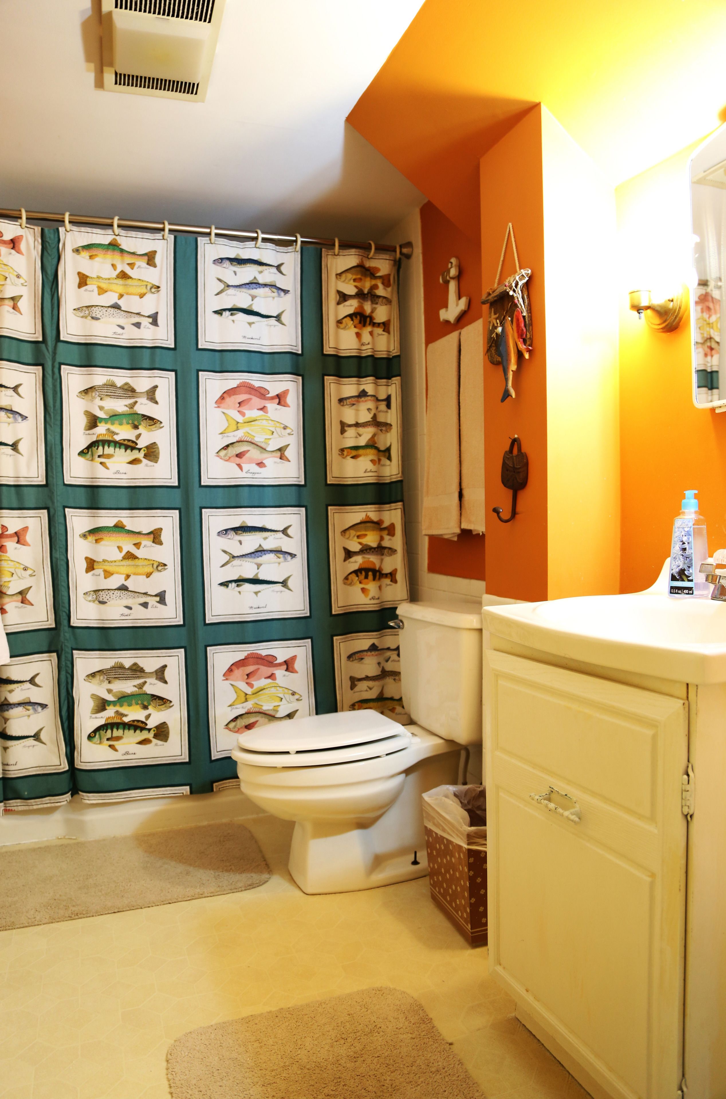 Une salle de bain équipée de toilettes, d’un lavabo et d’un rideau de douche orné d’illustrations de poissons.