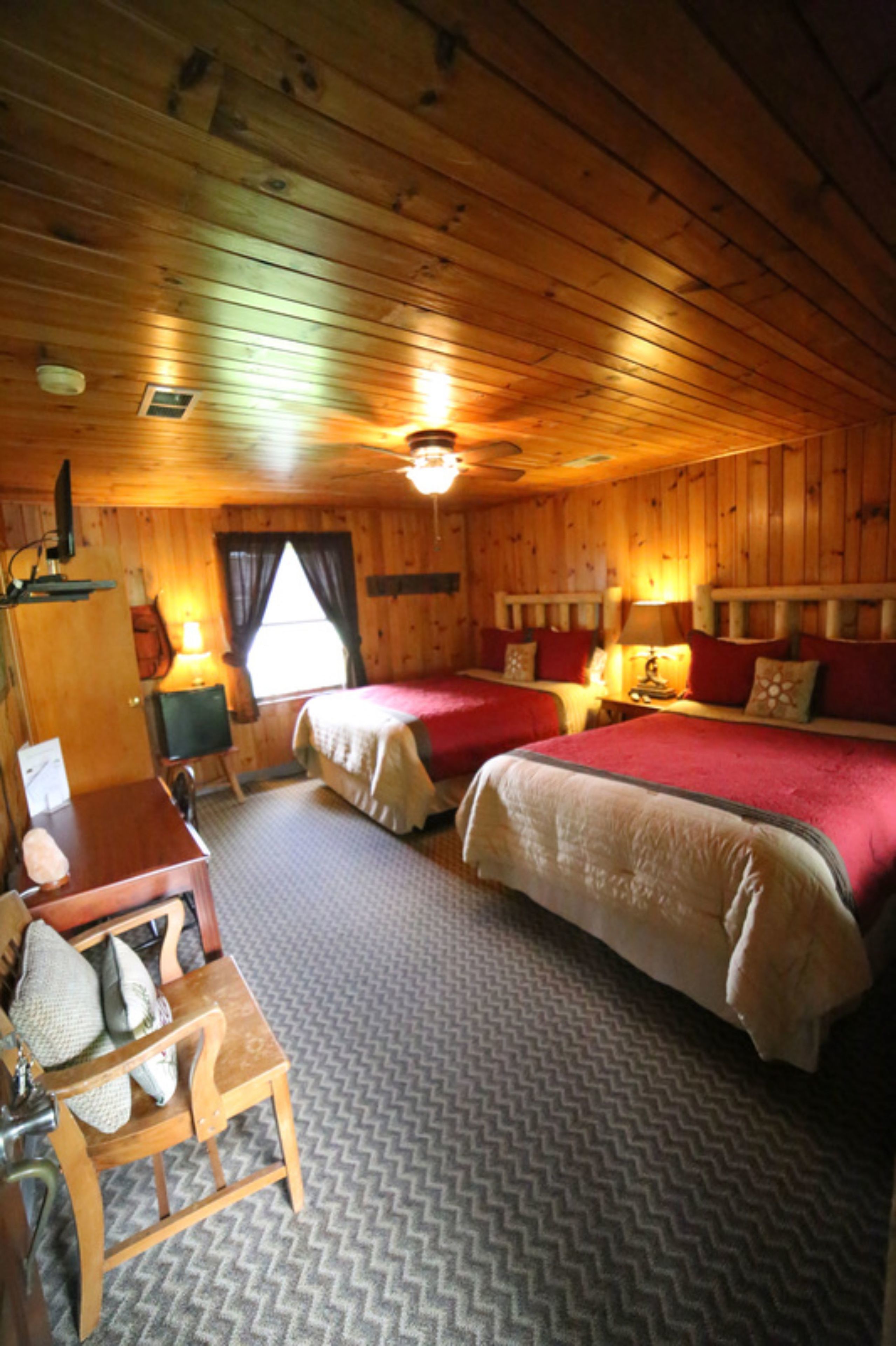 A cabin-style room with two beds, a wooden desk, and a chair.