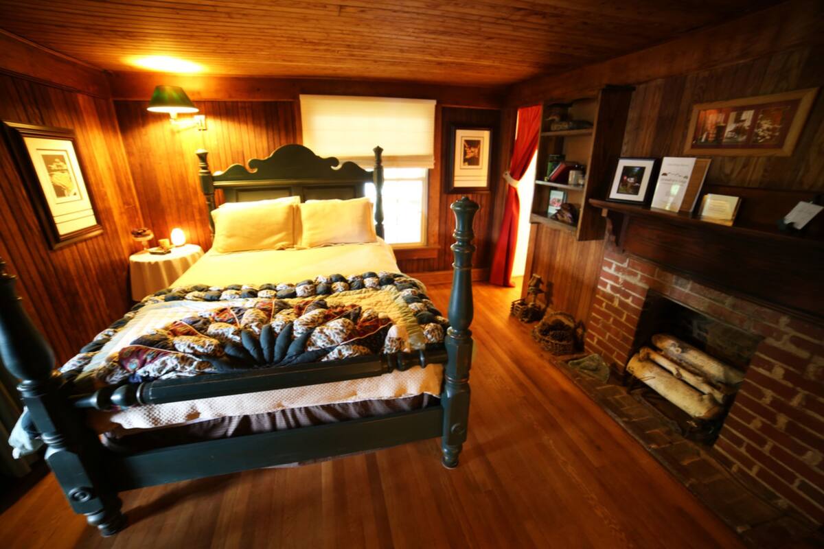 A traditional wooden room with a four-poster bed, a fireplace, and framed pictures on the walls.