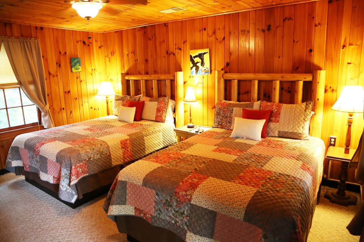 A room with two beds, wooden walls, and a window with curtains.
