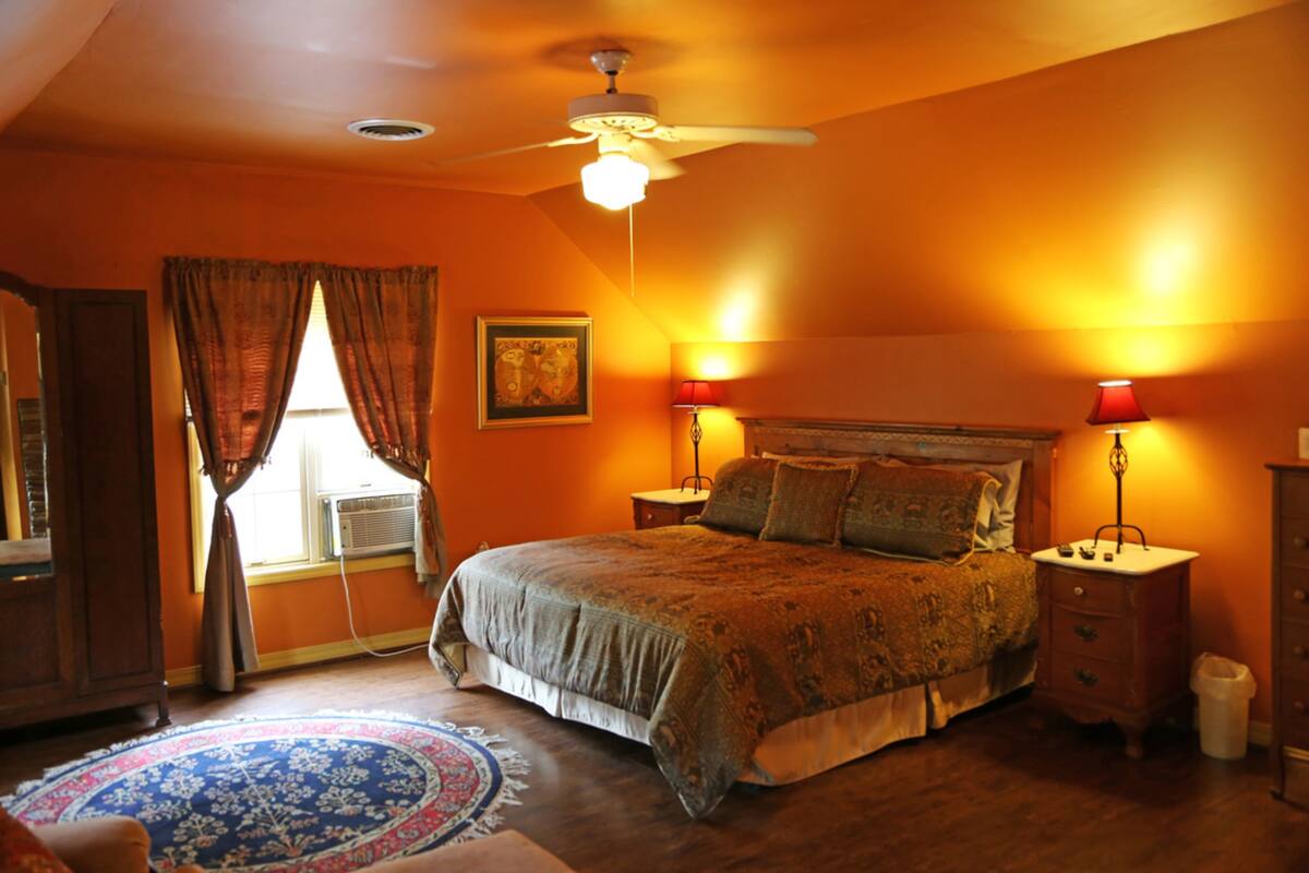 A bedroom with a bed, two bedside tables, a nightstand, a ceiling fan, and a window with curtains.