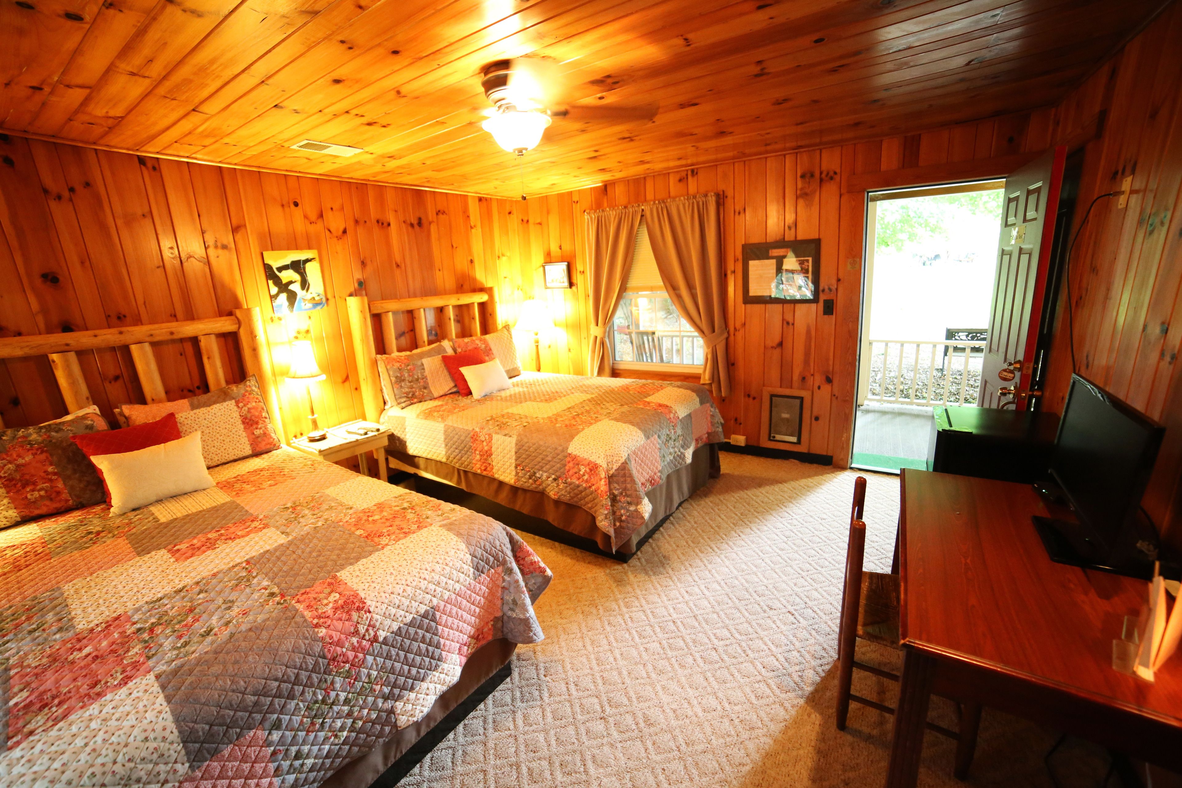 A cozy cabin-style room with two beds, a wooden dining table, and a television.