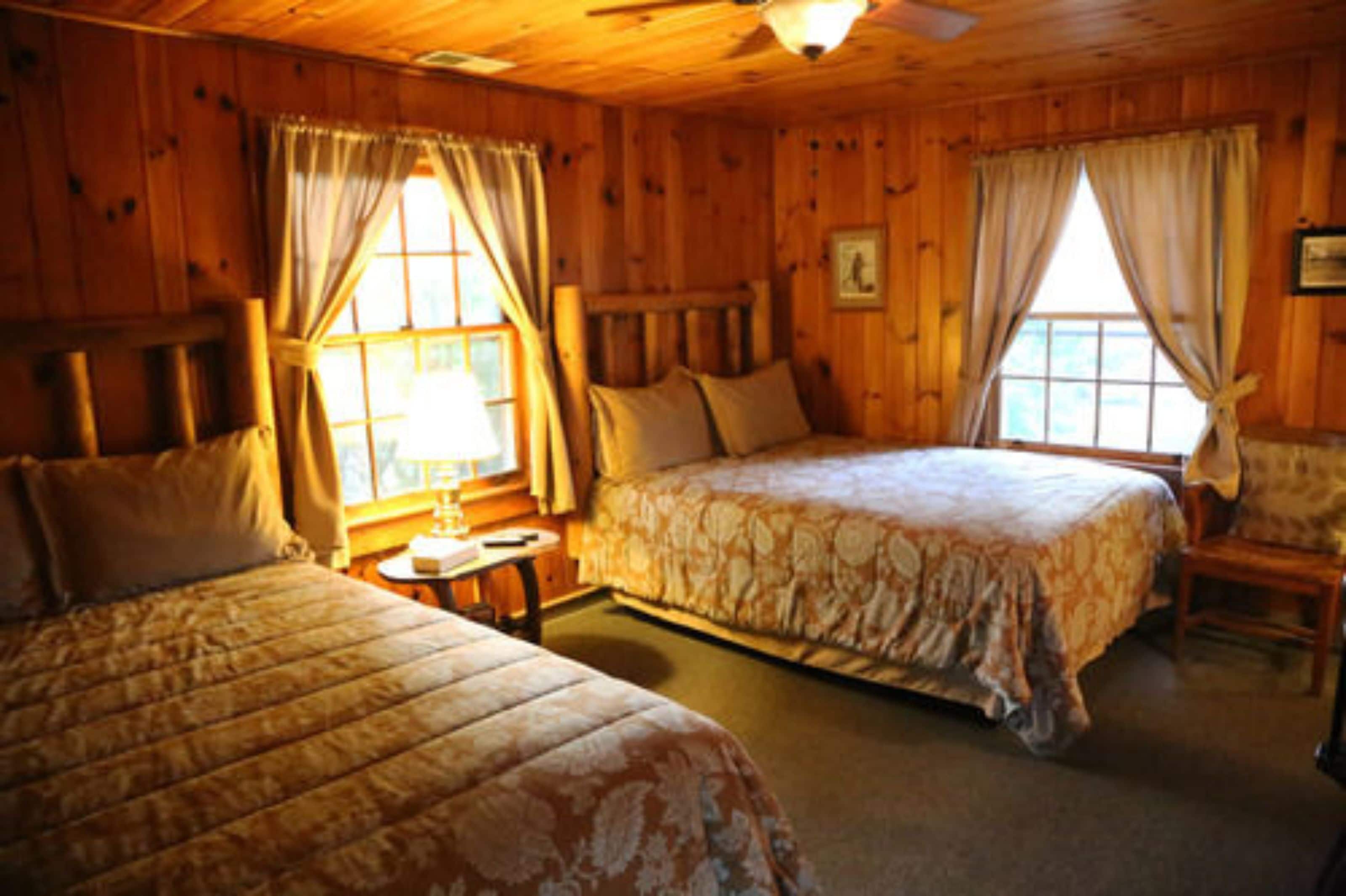 A wooden cabin bedroom with two beds, a small table, and a chair.