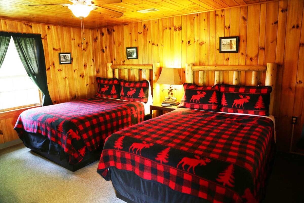 A cabin with two beds, wooden walls, and a ceiling fan.