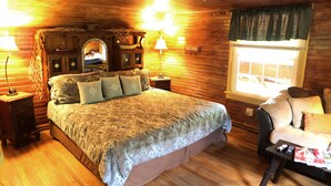 Ein gemütliches Schlafzimmer in einer Holzhütte mit einem großen Bett, zwei Nachttischen, einem Sessel und einem Fenster mit Vorhängen.