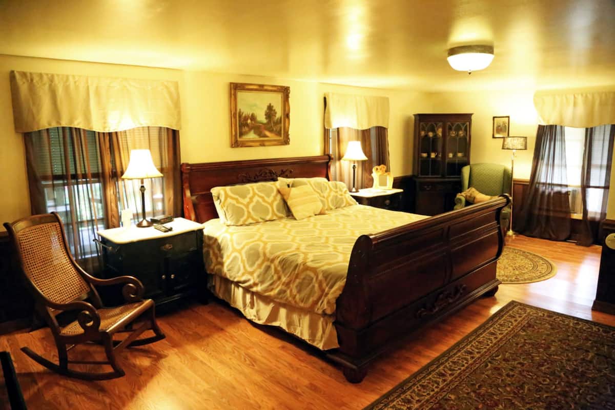 A traditional bedroom with a large bed, wooden headboard, a rocking chair, a dresser, and a cabinet.