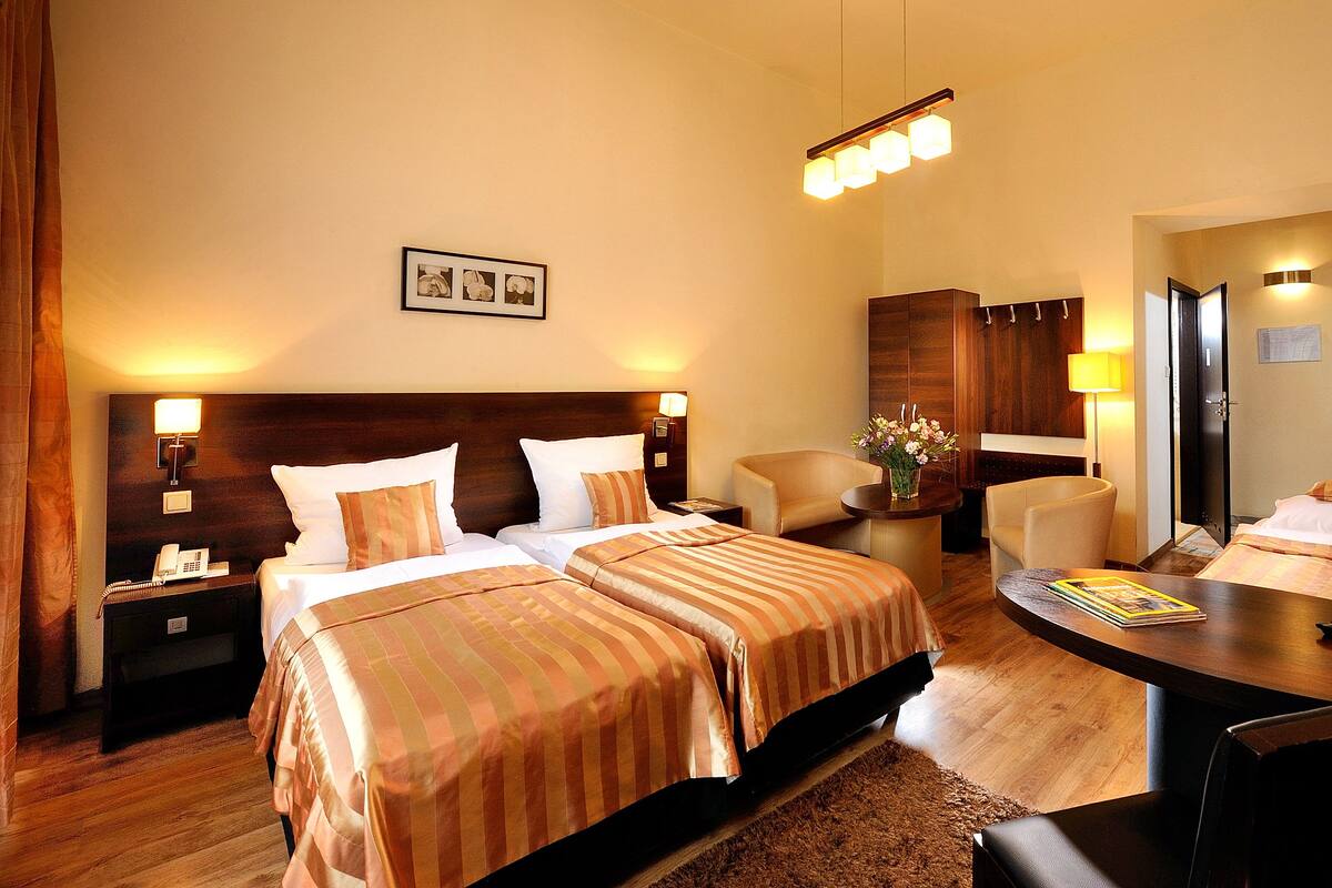 A hotel room with two beds, a desk, a chair, a nightstand, a lamp, and a mirror.