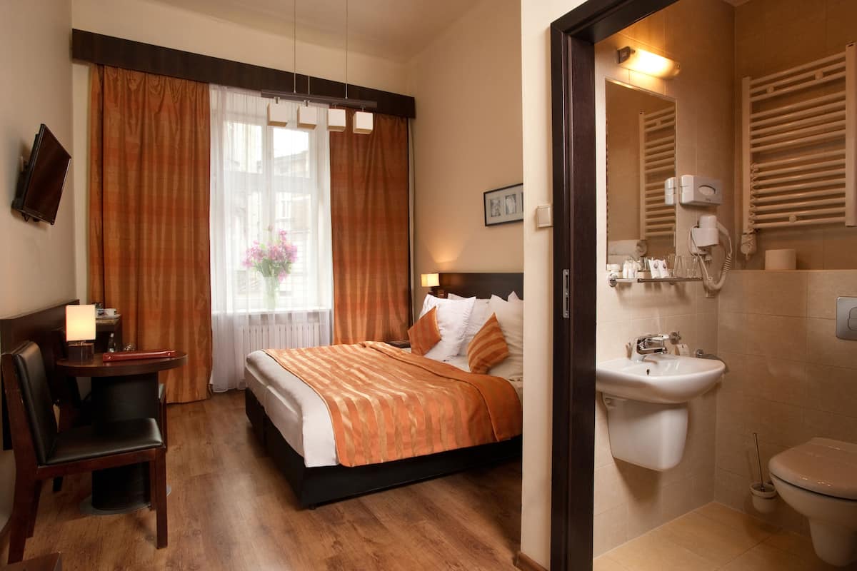 A hotel room with a bed, a desk with a chair, a window with curtains, a bathroom with a sink and toilet.