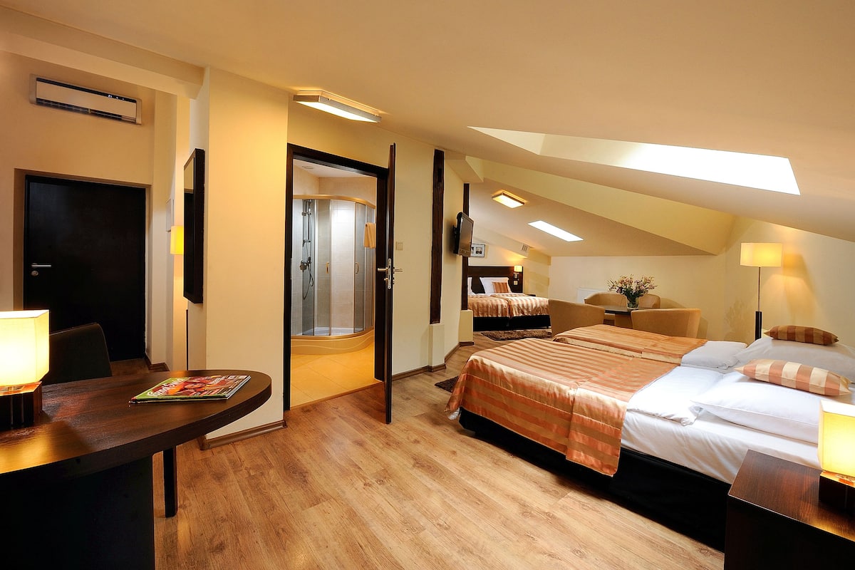 A hotel room with two beds, a desk, a TV, and a shower.