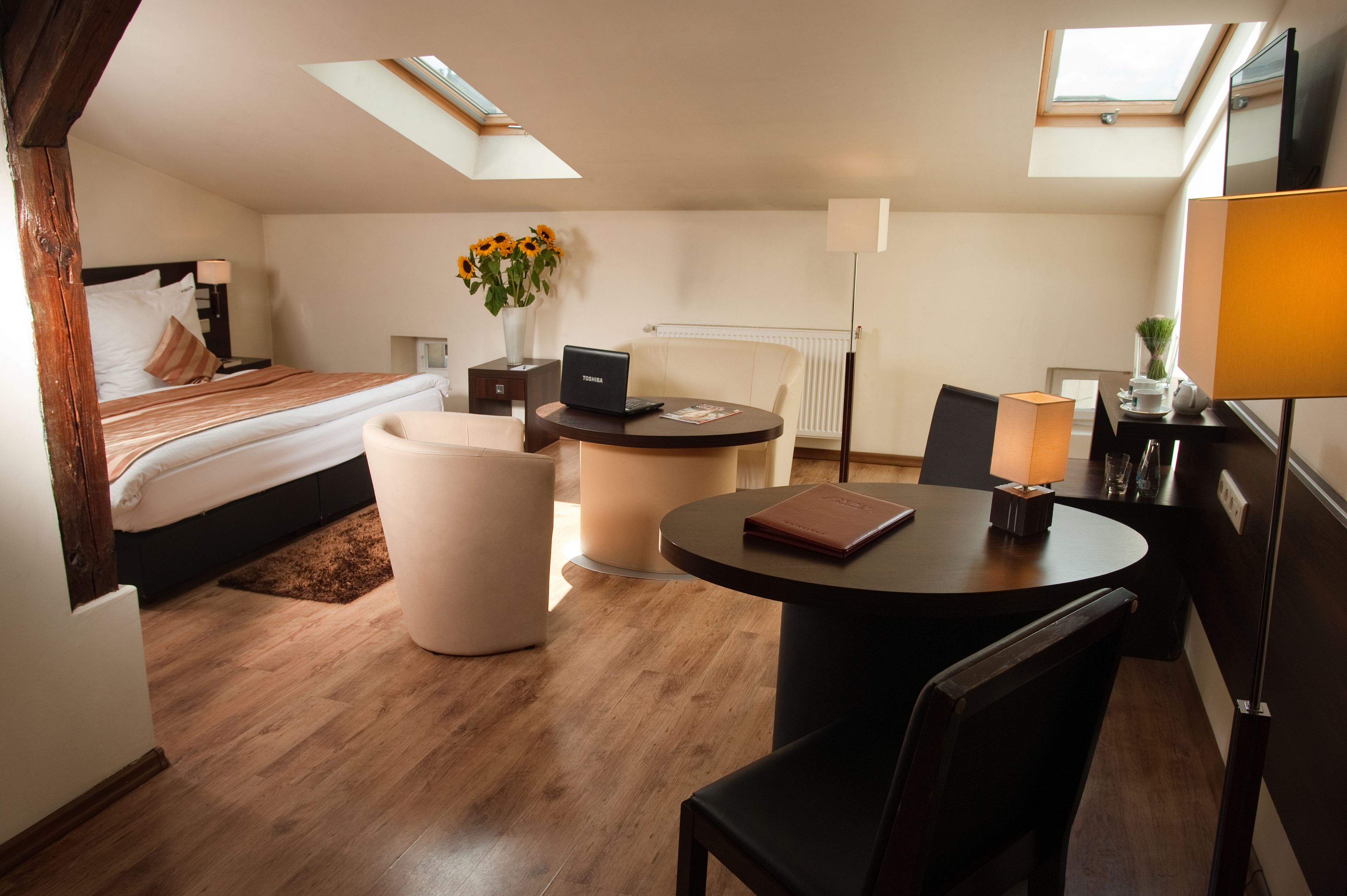 Une chambre d’hôtel comprenant un lit, un bureau, une chaise, une table, une lampe, un radiateur et une fenêtre.