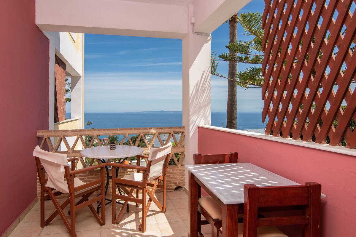 A balcony with a table and chairs, a view of the sea, and a wooden lattice.