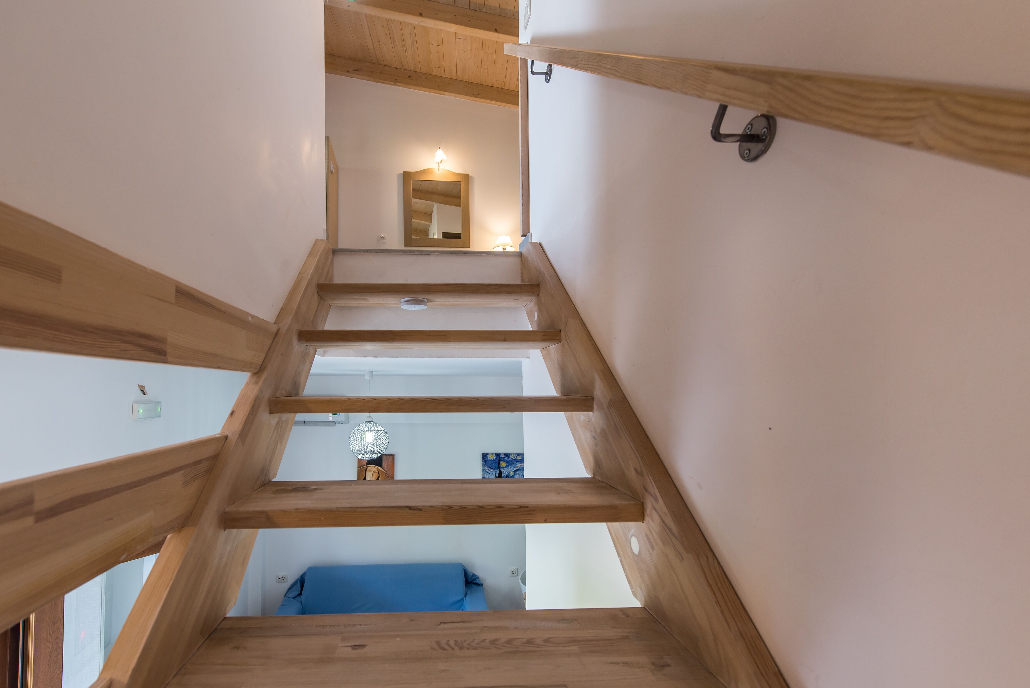 A wooden staircase leading to a room with a blue sofa, a lamp, and a painting on the wall.