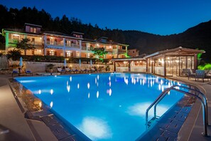 A swimming pool with a clear blue water surface, surrounded by lounge chairs and umbrellas. - Sea View Village - Studios & Apartments (Zakynthos)