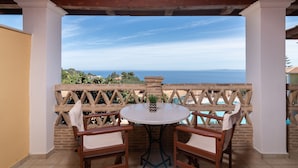 Un espacio de estar al aire libre cubierto con mesa y sillas, con vistas panorámicas al mar y las colinas.
