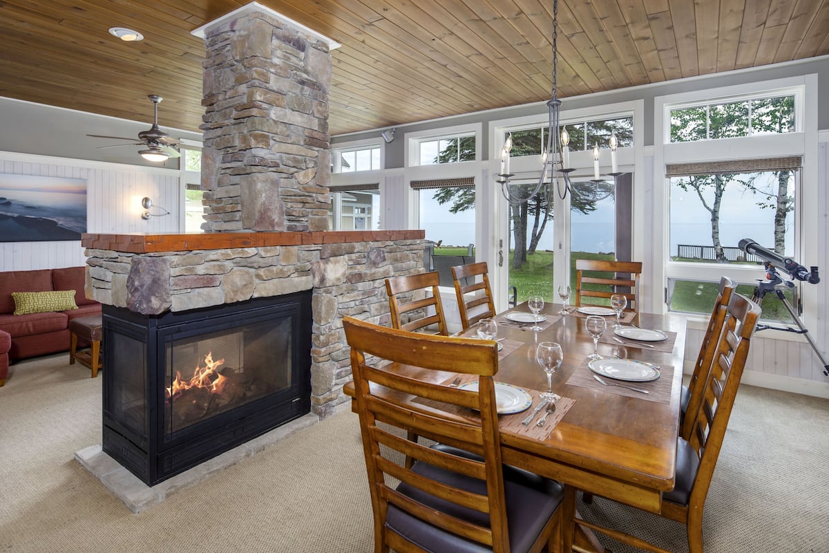 A dining area with a stone fireplace, wooden chairs, and a table set for four.