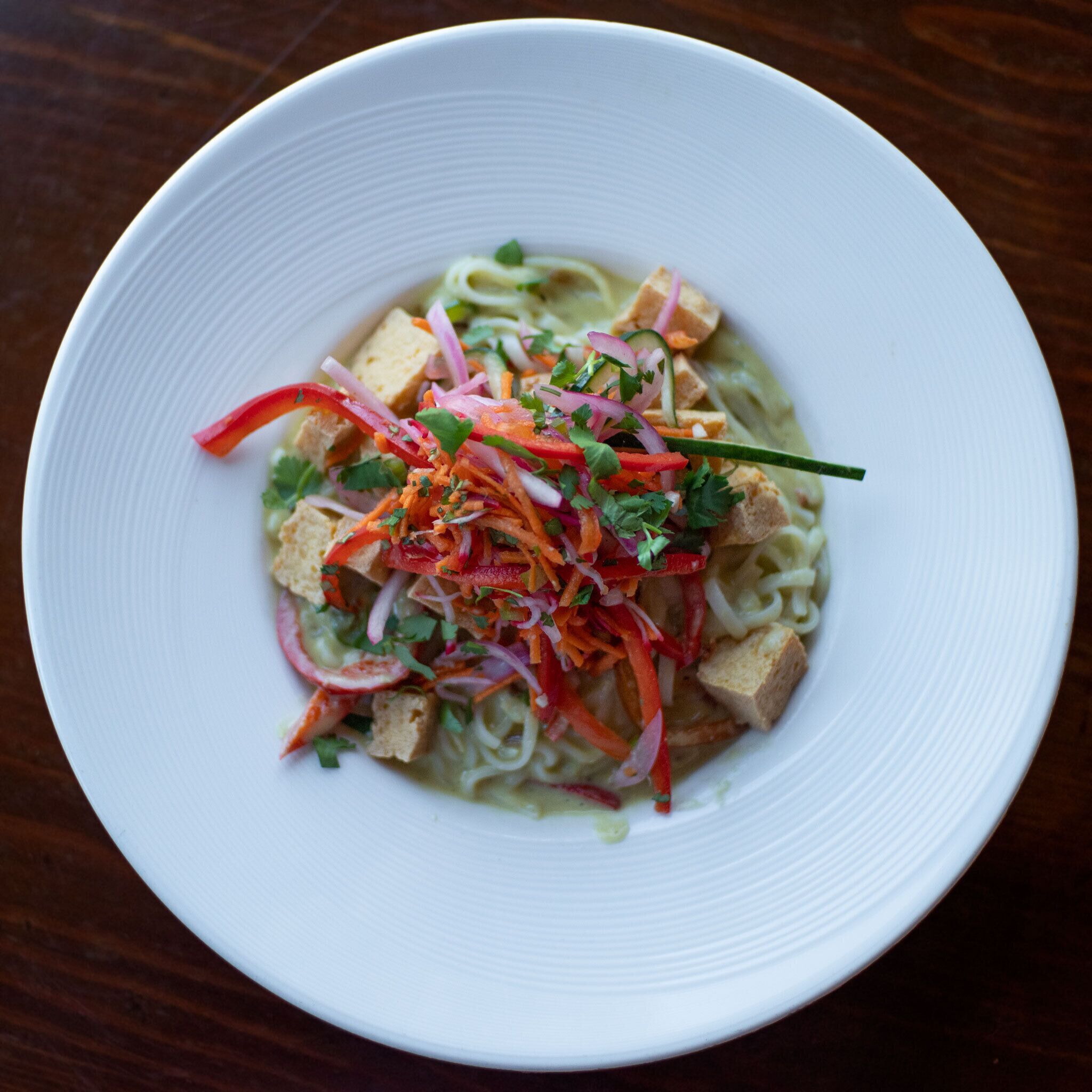 A bowl of noodle soup with vegetables and tofu on a white plate.