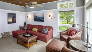 Una sala de estar acogedora con un sofá sectional rojo, un sillón de cuero marrón, una mesa de centro de madera y una mesita auxiliar de mimbre.