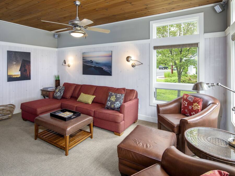 Una sala de estar acogedora con un sofá sectional rojo, un sillón de cuero marrón, una mesa de centro de madera y una mesita auxiliar de mimbre.
