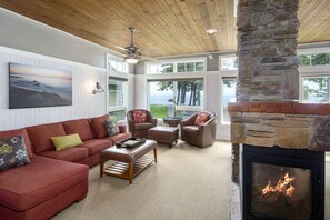 A cozy living room with a stone fireplace, a red sofa, and a view of the outdoors. - Larsmont Cottages (Two Harbors)