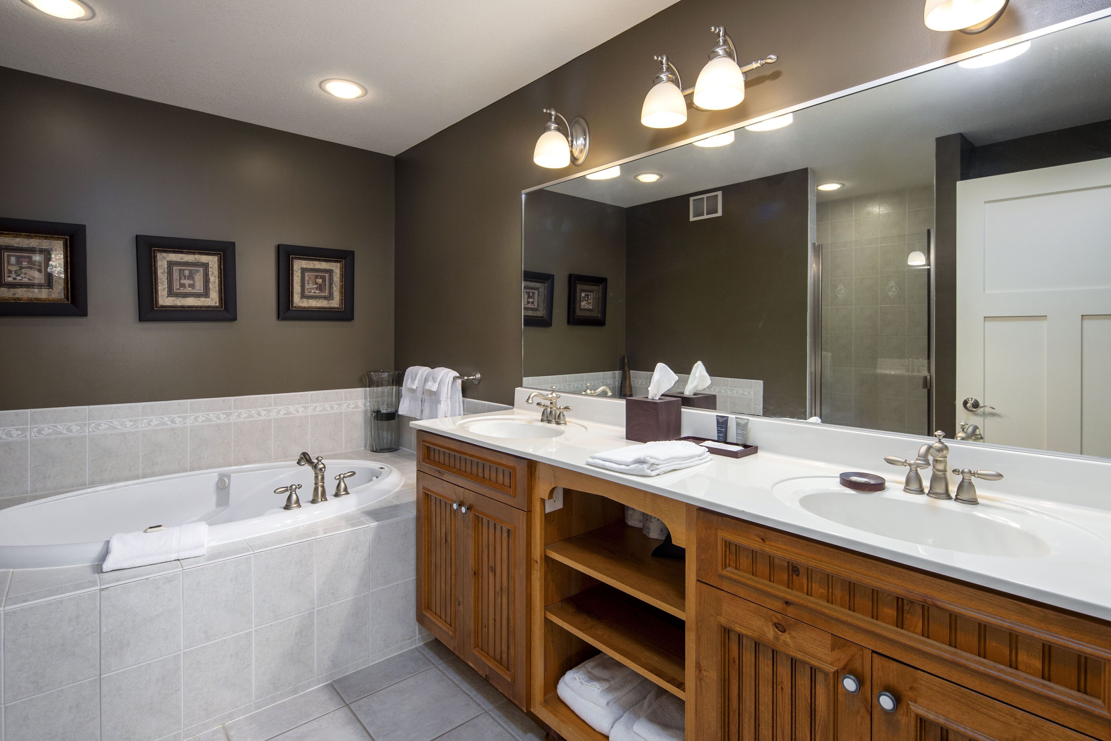 A modern bathroom with a large bathtub, two sinks, wooden cabinetry, and a large mirror.