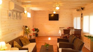 A cozy wooden cabin interior with a sofa, chairs, a dining table, and a TV mounted on the wall. - Hotel Villa Monte (Kemer)