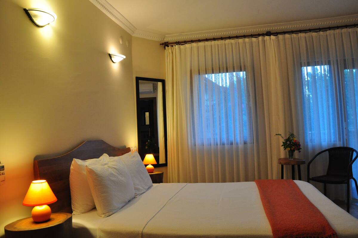A hotel room with a bed, two bedside lamps, a nightstand, a chair, and a window with curtains.