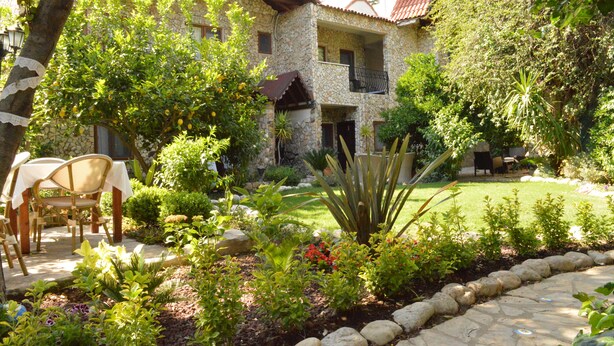 A stone house with a balcony, surrounded by a garden with various plants and a lawn. - Hotel Villa Monte (Kemer)