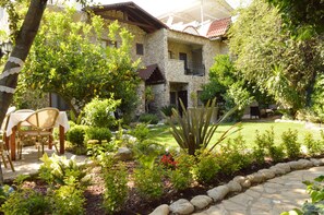 A stone house with a balcony, surrounded by a garden with various plants and a lawn. - Hotel Villa Monte (Kemer)