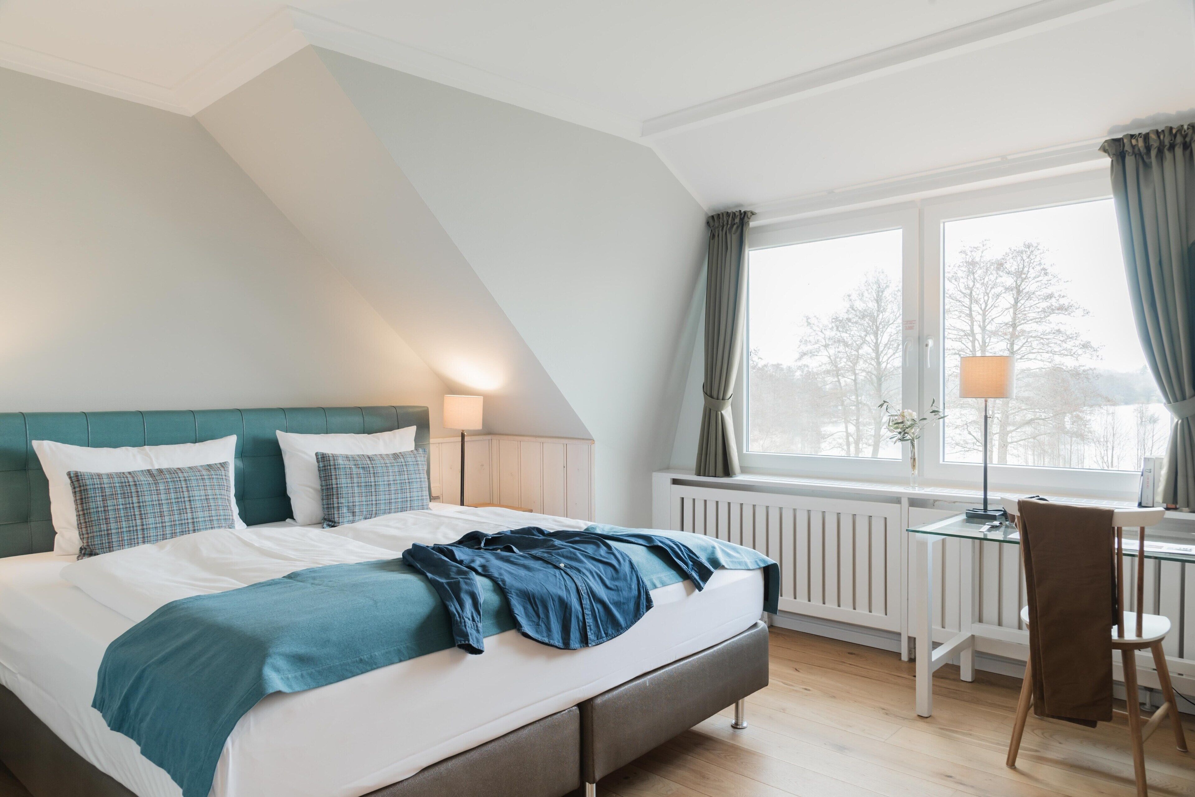 A bedroom with a bed, a desk, and a window with curtains.